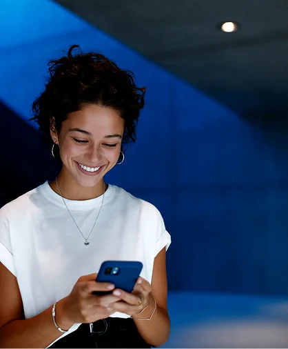 Mulher sorridente segurando celular em ambiente moderno, representando estratégia de redes sociais e conteúdo digital